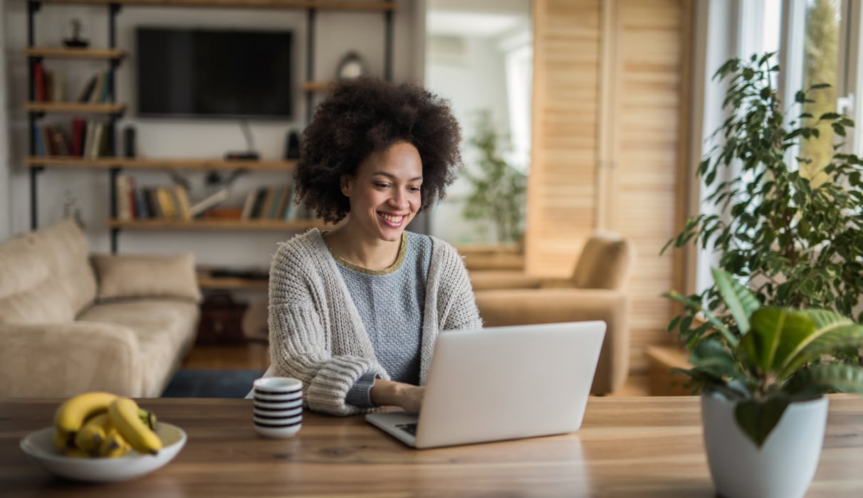 Woman smiling, sitting at a table with her laptop and cup