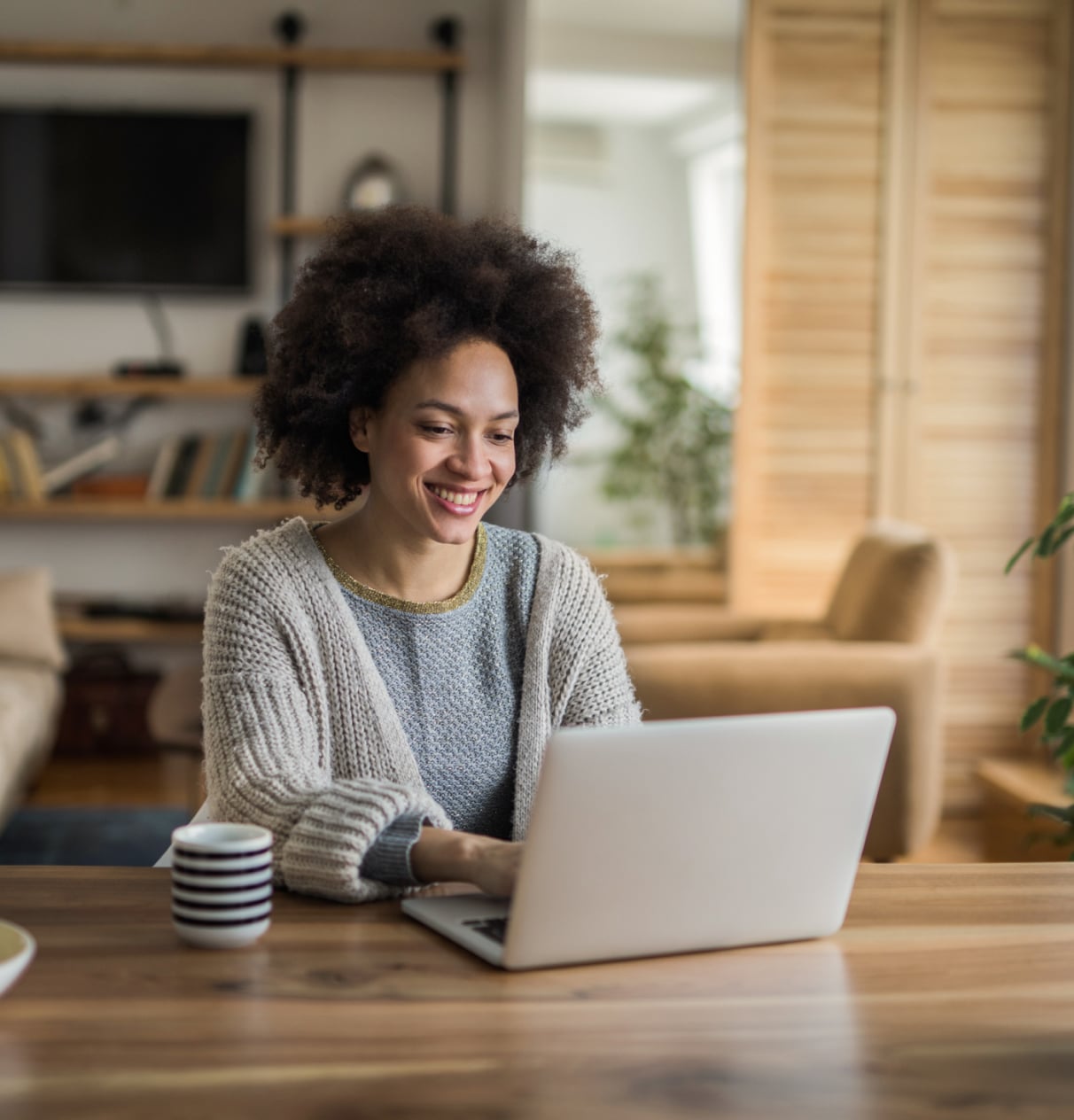 Woman smiling, sitting at a table with her laptop and cup