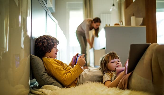 Children using tablet devices while mother is  in the background