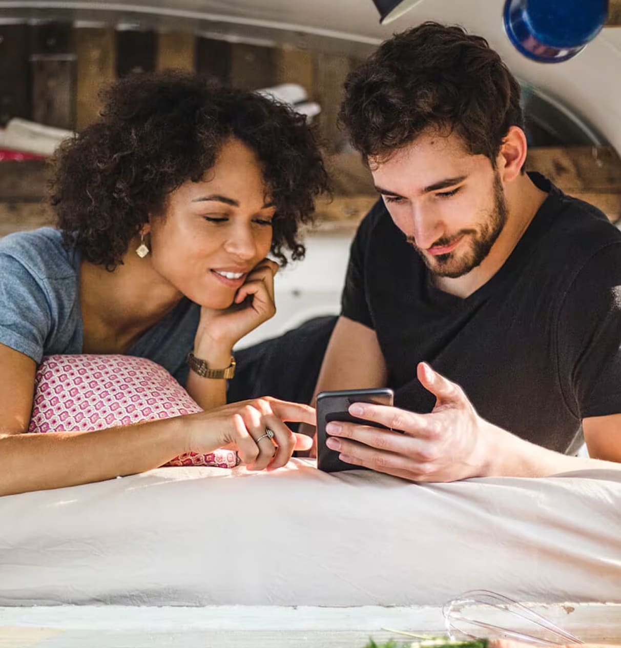 Man and woman lying on bed both looking at a mobile screen together